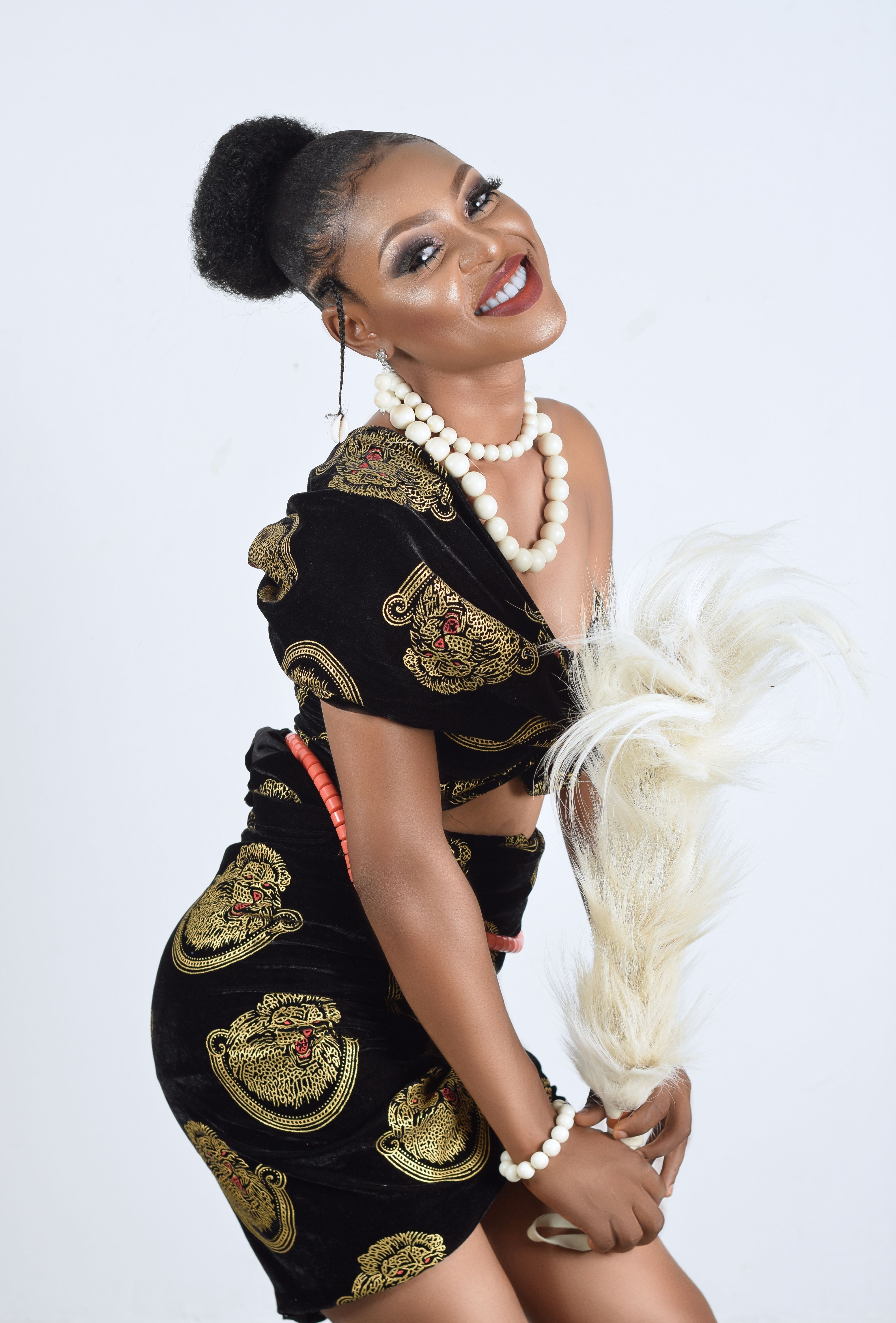 Smiling woman in fashionable black dress and pearl jewelry in studio setting.