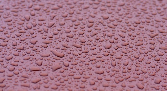 A detailed macro shot of raindrops on a wet pink surface, creating an abstract texture.