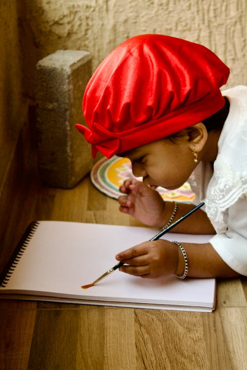 Free A child wearing a red hat is drawing on a piece of paper Stock Photo