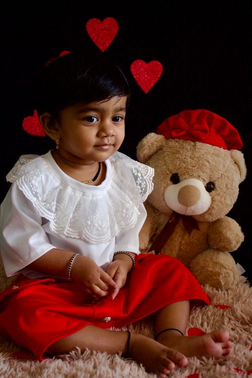 Free Cute child sitting with teddy bear and red hearts, symbolizing innocence and joy. Stock Photo