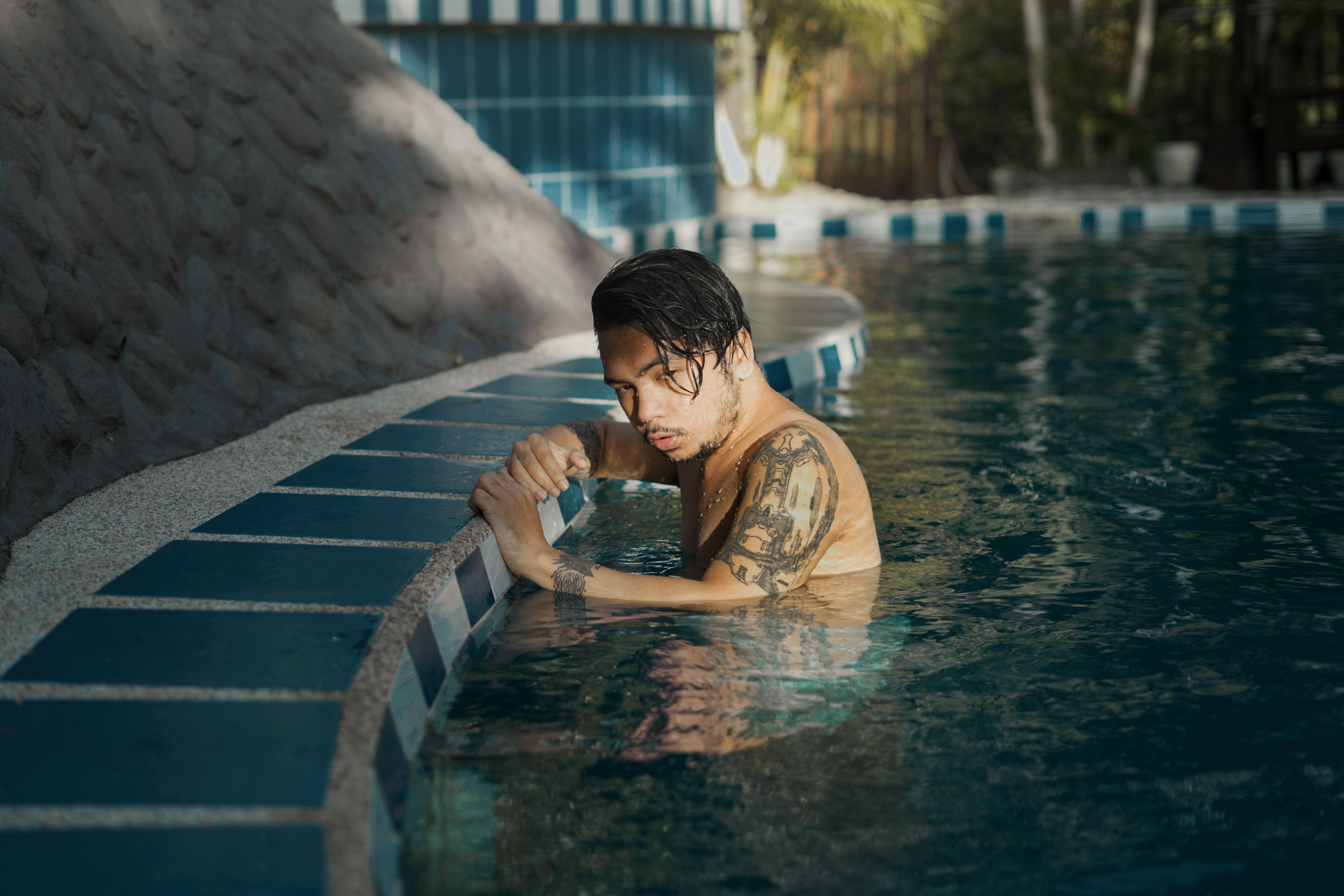 A young man with tattoos relaxing in a sunlit swimming pool.