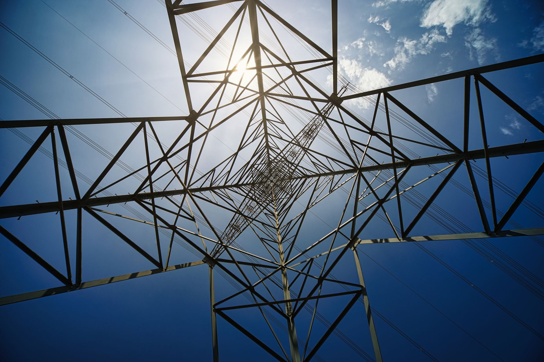 Looking up at a high voltage transmission tower silhouetted against a blue sky and bright sun.