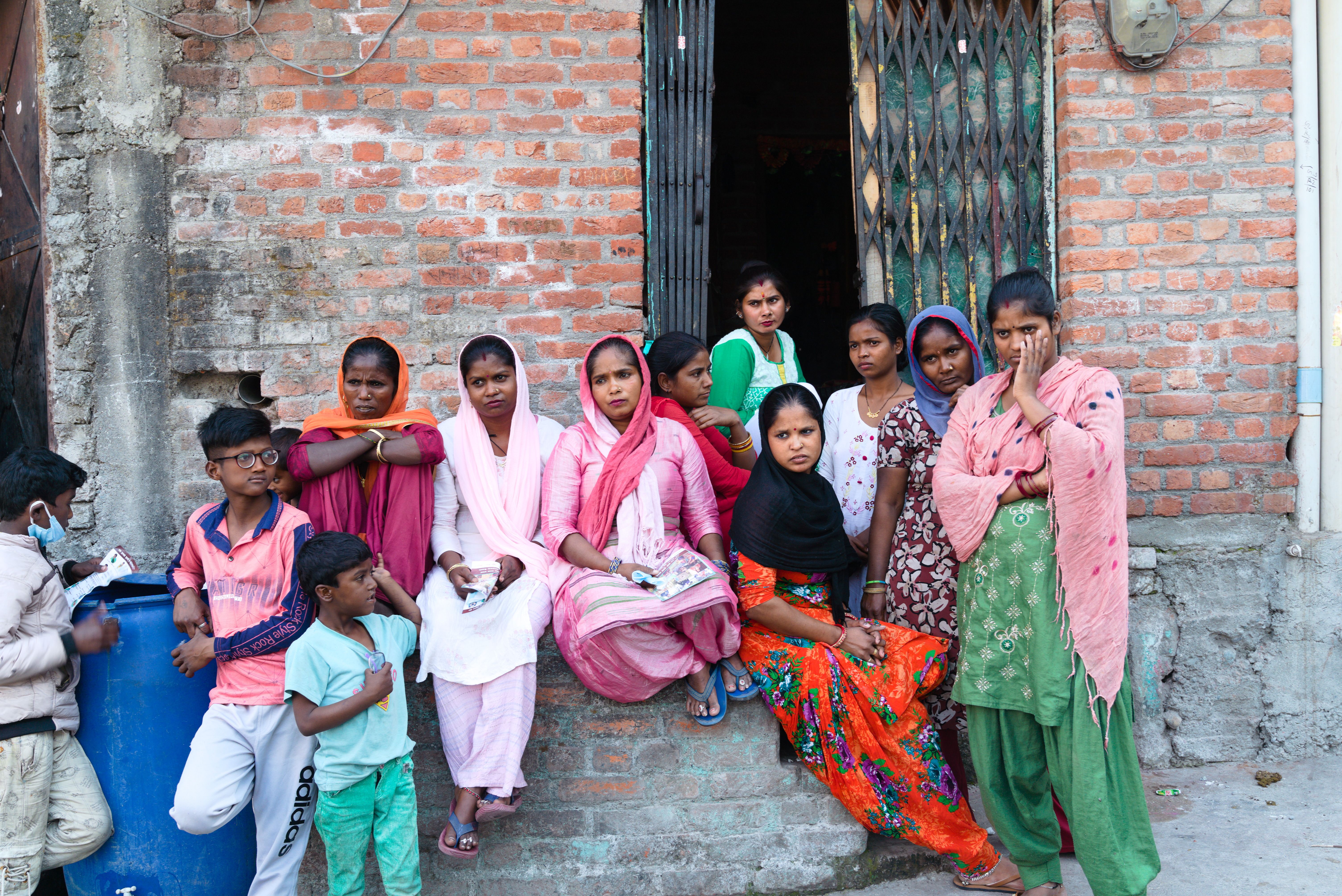 A vibrant group sits outside a brick house in rural Haldwani, India, showcasing local lifestyle.