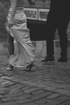 A couple elegantly moving on cobblestone in an urban black and white photo.