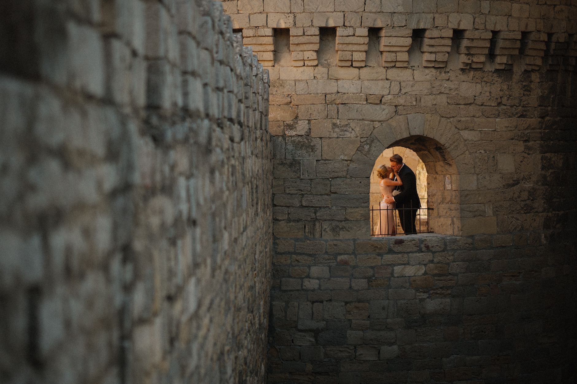 A romantic moment captured as newlyweds kiss within an ancient stone castle window.