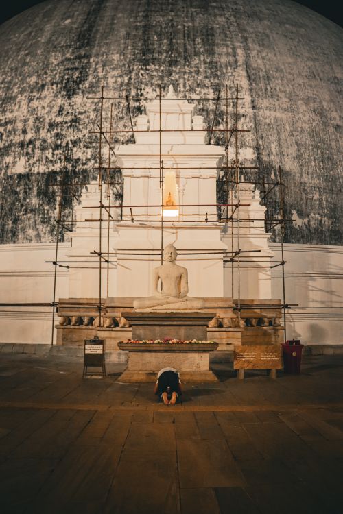Free A person prays before a Buddhist statue at a historic stupa, lit warmly at night. Stock Photo