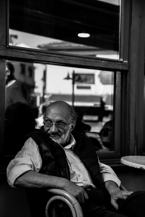 Free A candid black and white portrait of an elderly man relaxing by a cafe window, reflecting tranquility. Stock Photo