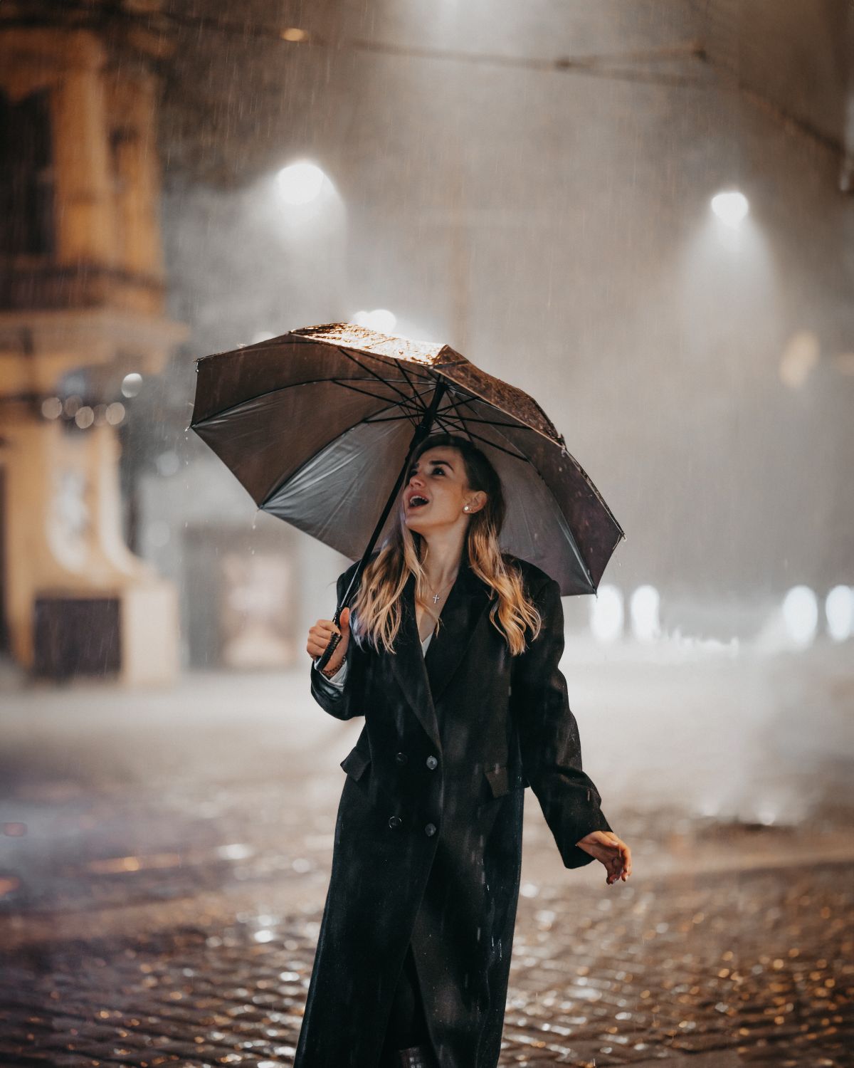 Young woman in a coat standing under an umbrella on a street in heavy rain