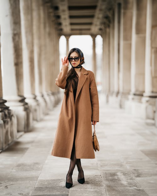 Fotos de stock gratuitas de abrigo largo marrón, arreglando gafas de sol, columnata