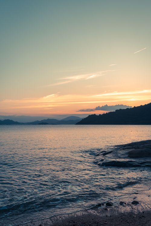 Free Vibrant sunset over the ocean with silhouettes of distant mountains. Perfect for coastal scenery lovers. Stock Photo