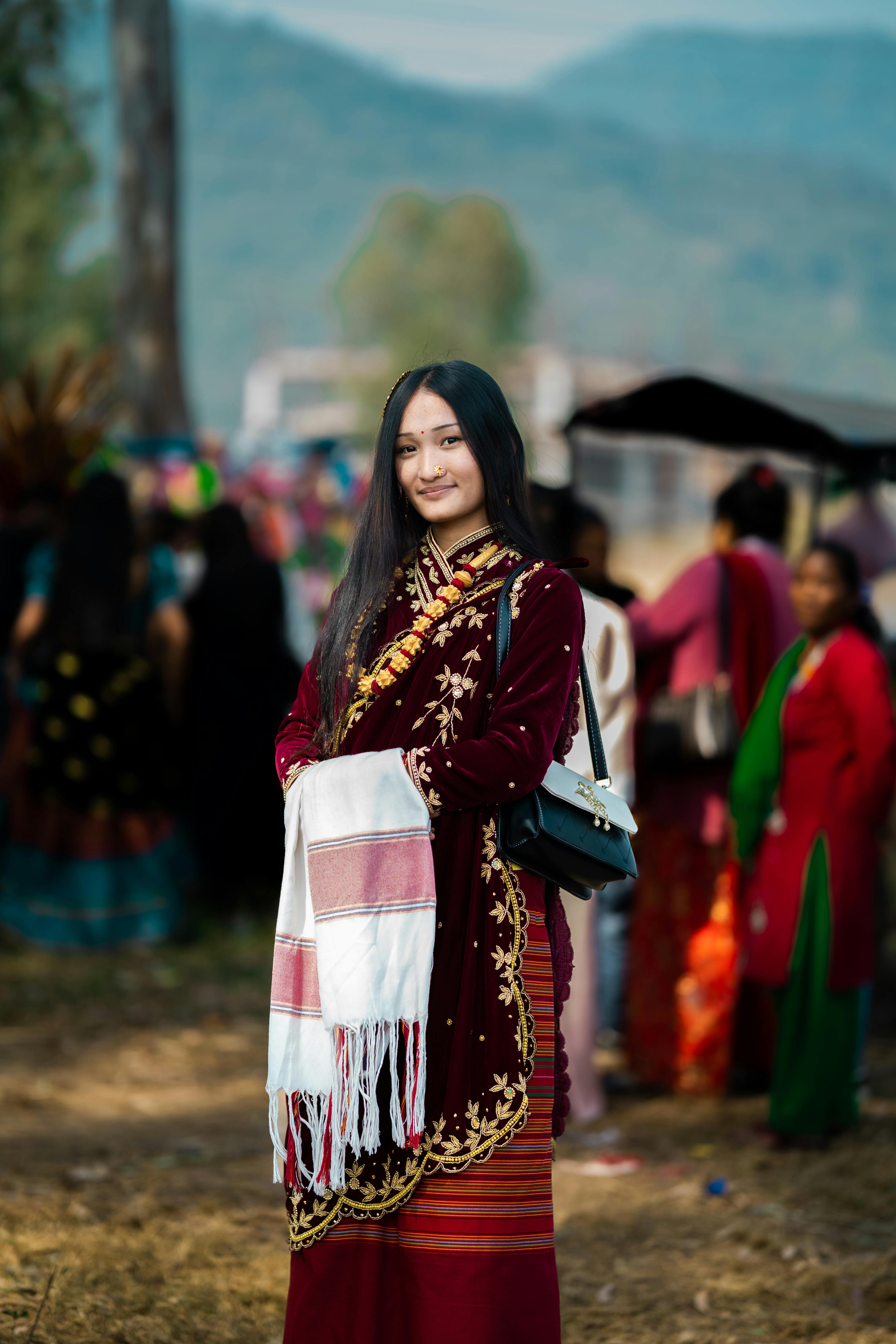 Asian woman in intricate traditional attire at a lively outdoor festival.