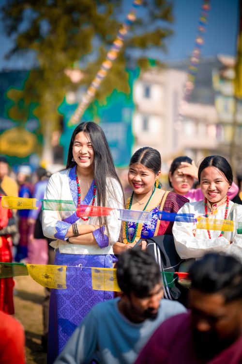 Free Three women in colorful traditional clothing smiling at a vibrant outdoor festival. Stock Photo