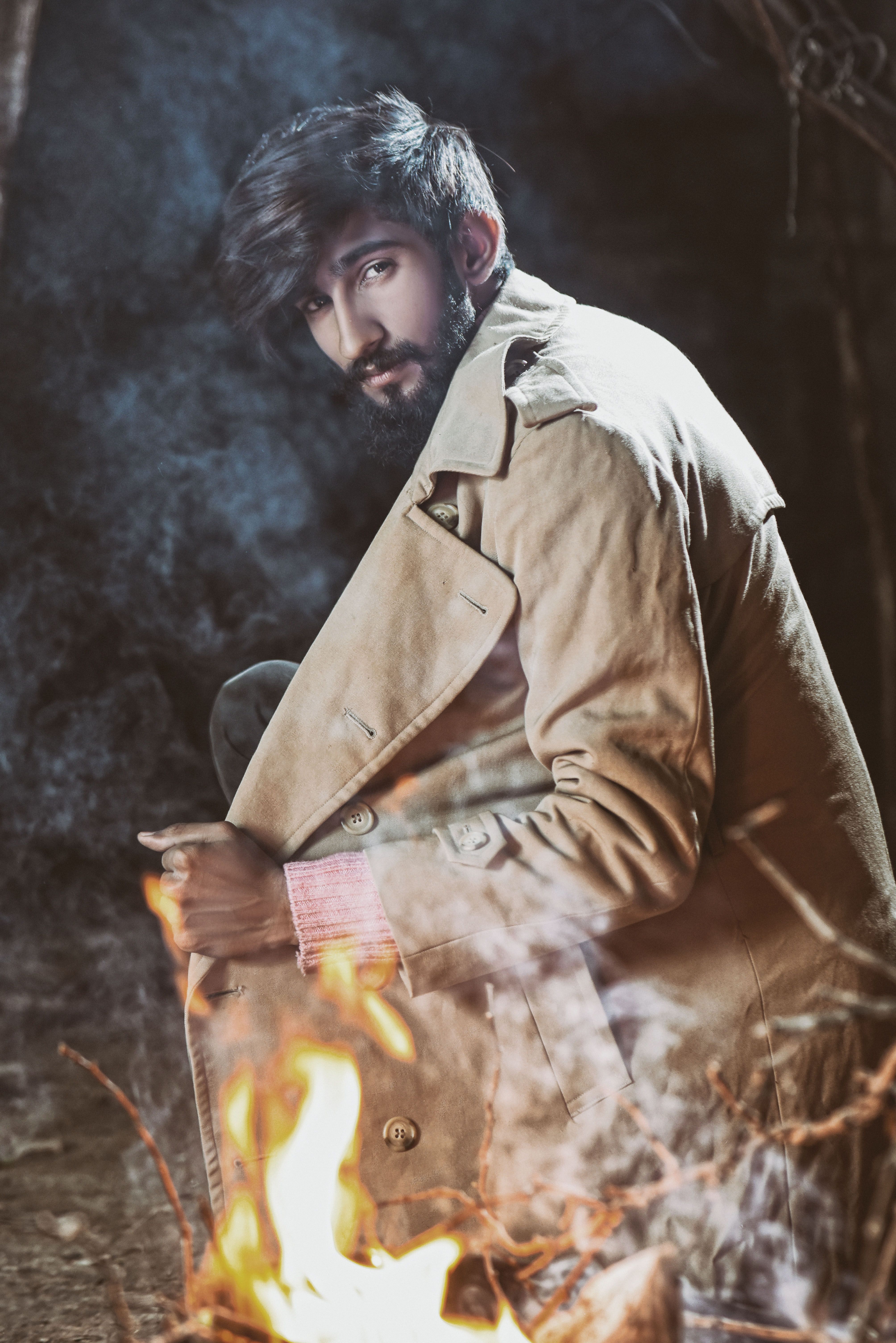 Portrait of a man in a coat crouching by a campfire at night in Islamabad.