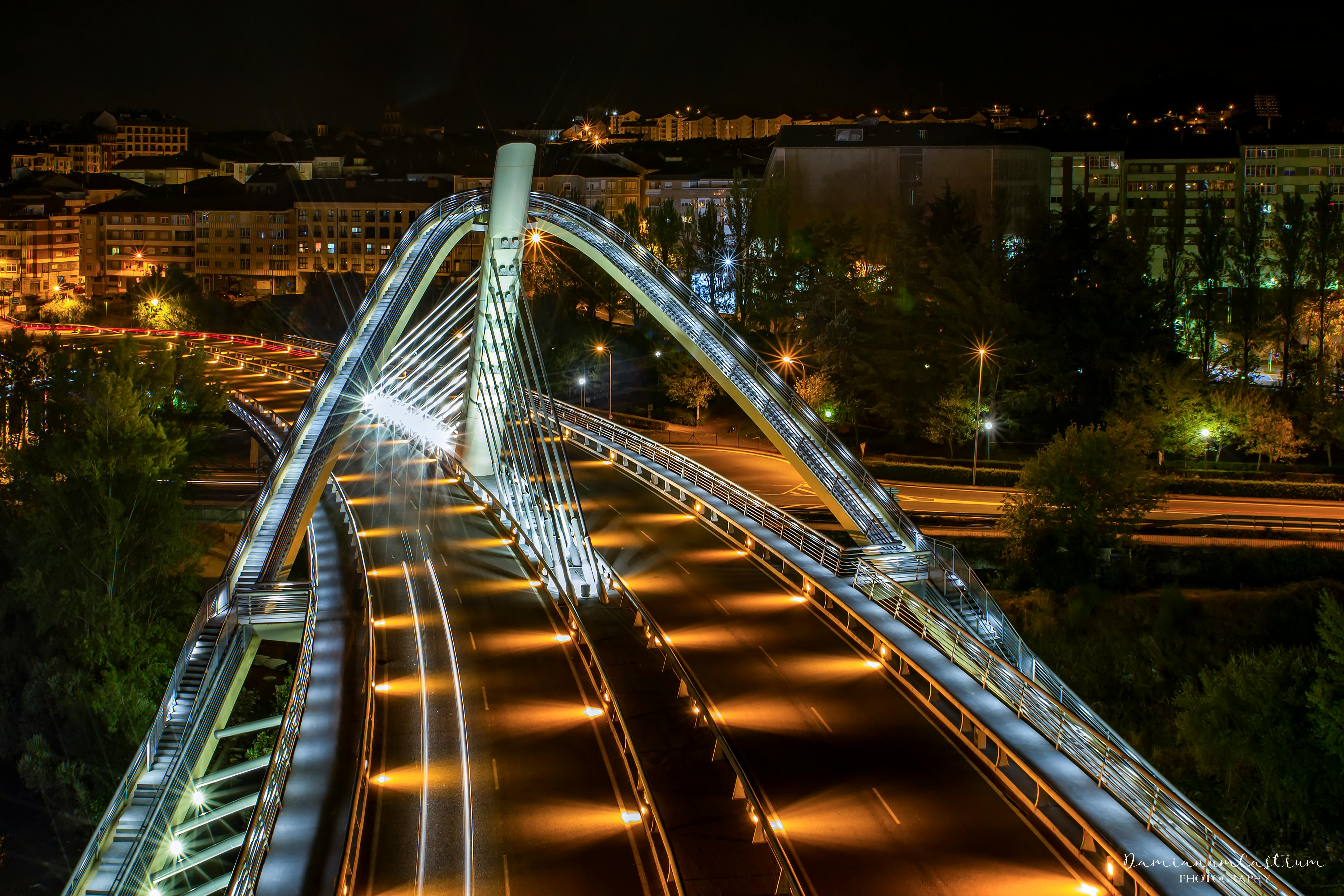 Majestic night view of the illuminated Ponte do Milenio bridge in Ourense, Spain, showcasing urban lights and architectural beauty.