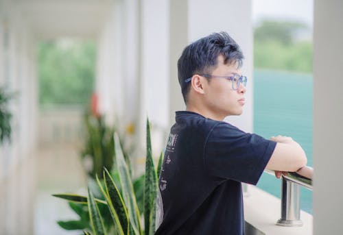 Young Man in Blue Eyeglasses Standing on the Balcony