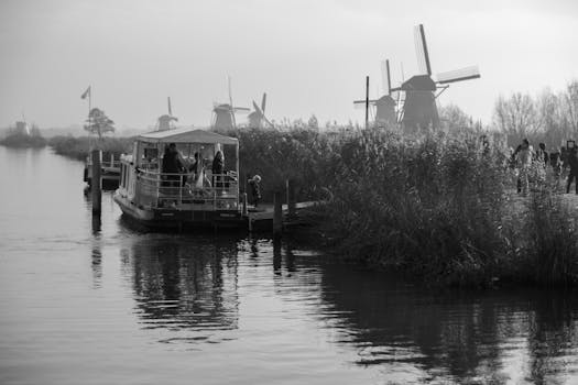 Black and white image of Kinderdijk's iconic windmills with boat and reflections.