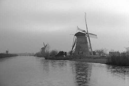 A black and white photo of a windmill on a river