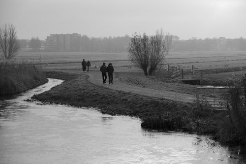 Free Serene black and white scene of people walking along a misty river path in Kinderdijk, Netherlands. Stock Photo