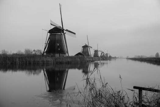 Black and white photo of Kinderdijk windmills reflecting in a serene canal in Holland.