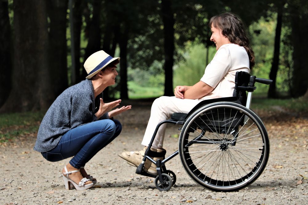 Dos jóvenes riendo y conversando en un parque soleado, una de ellas en silla de ruedas