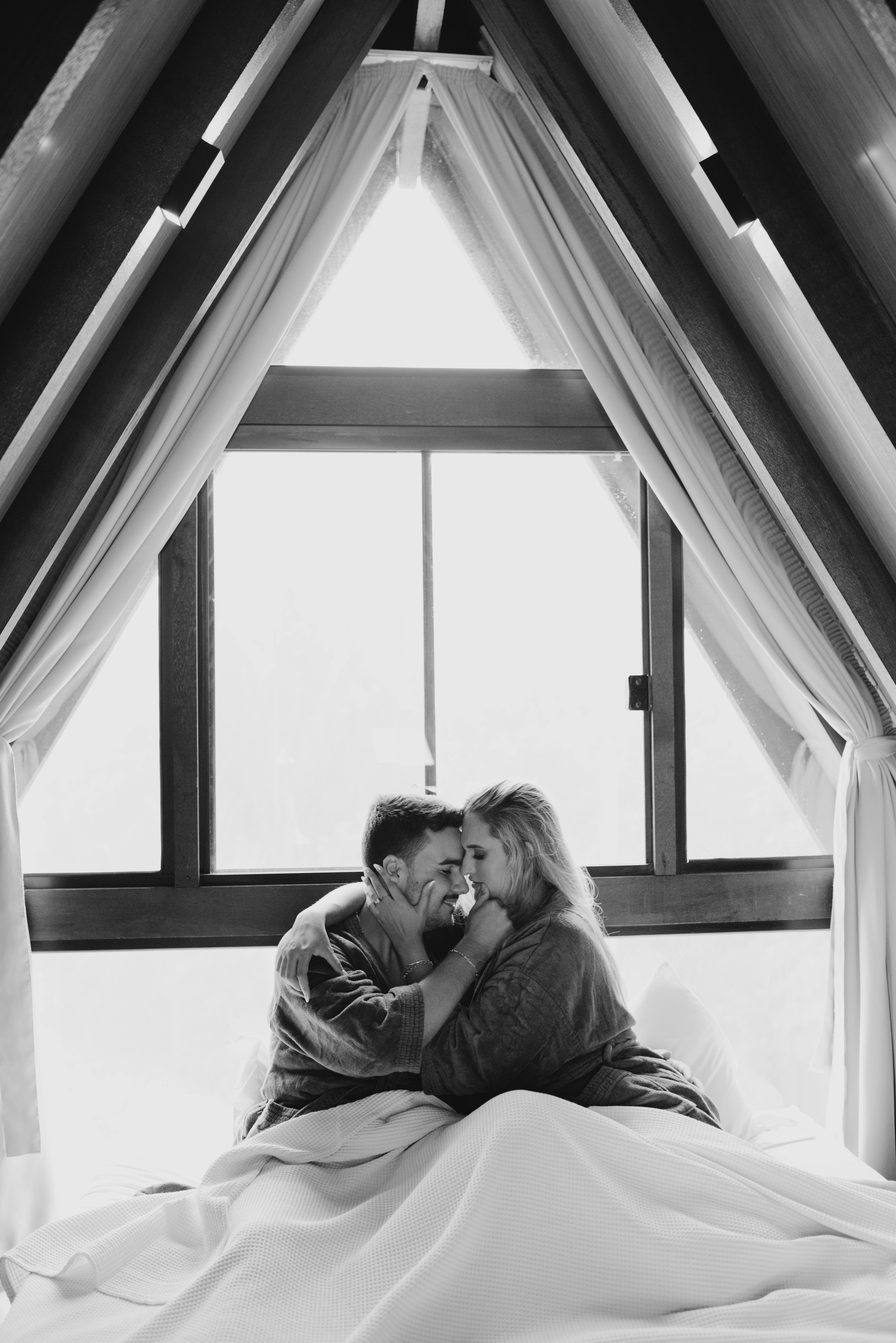 A couple sharing an intimate moment in black and white by a window indoors.