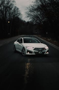 A white car driving through a dark, forested road, creating a mysterious atmosphere.