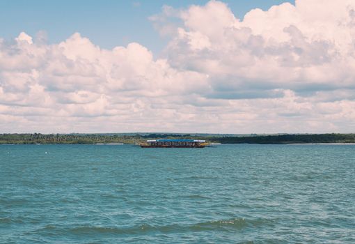 A serene view of a boat sailing on the ocean with fluffy clouds above in João Pessoa, Brazil.