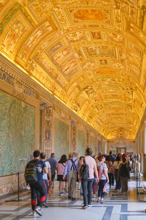 Free Visitors admiring the ornate ceilings and historic murals in Vatican City museum hall. Stock Photo