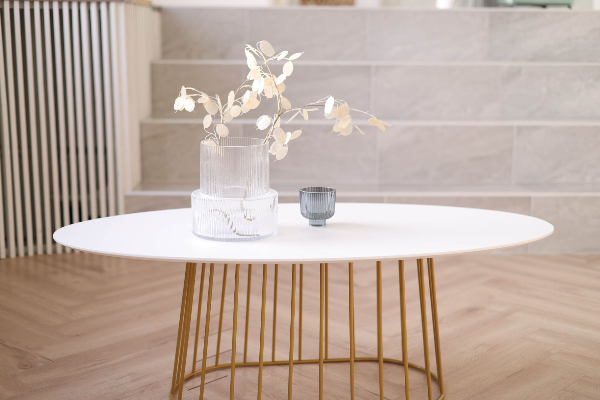 Contemporary white oval table with golden legs featuring elegant decor and vase for modern interior design.