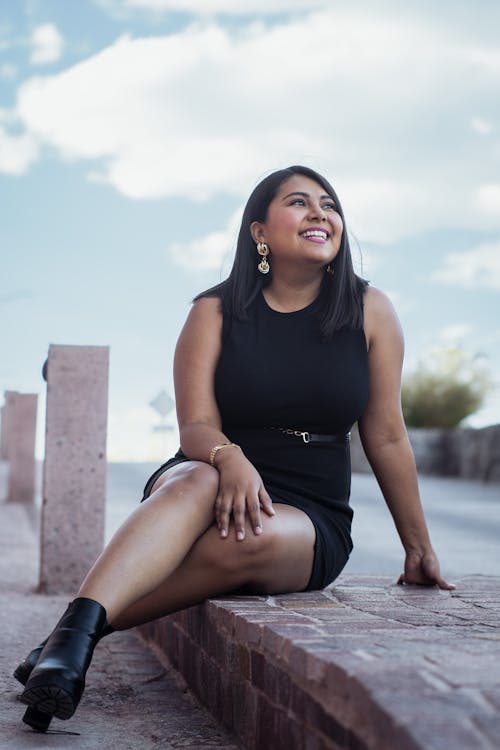 A woman in black dress sitting on a brick wall