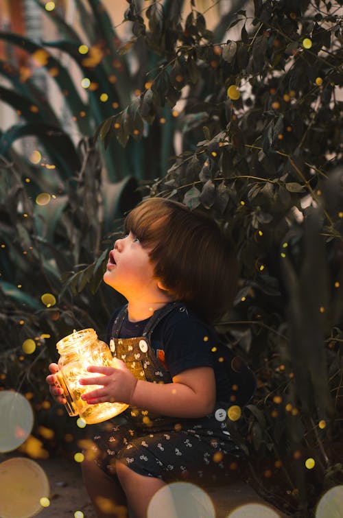 Ребенок держит прозрачную стеклянную банку с желтым светом