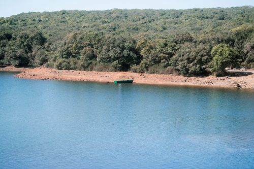 Free Tranquil scene of a lake with a forested hill backdrop and a boat on the shore. Stock Photo