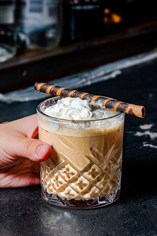 Close-up of a Person Holding a Glass with Iced Coffee with Whipped Cream