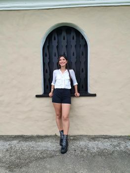 Confident young woman posing against a stylish wall on an urban street, exuding contemporary fashion vibes.
