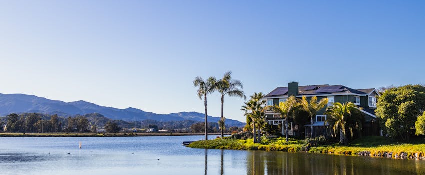 A beautiful lakeside mansion surrounded by palm trees under a clear blue sky.