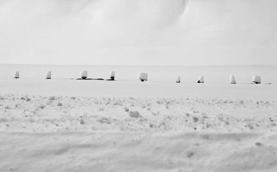 A serene snowy rural scene featuring snow-covered fence posts lined across a field.