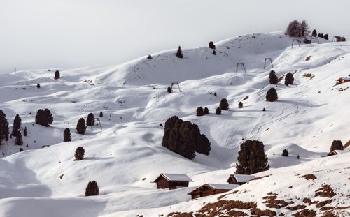 Free Serene winter scene of snow-covered hills with scattered trees and wooden cabins. Stock Photo