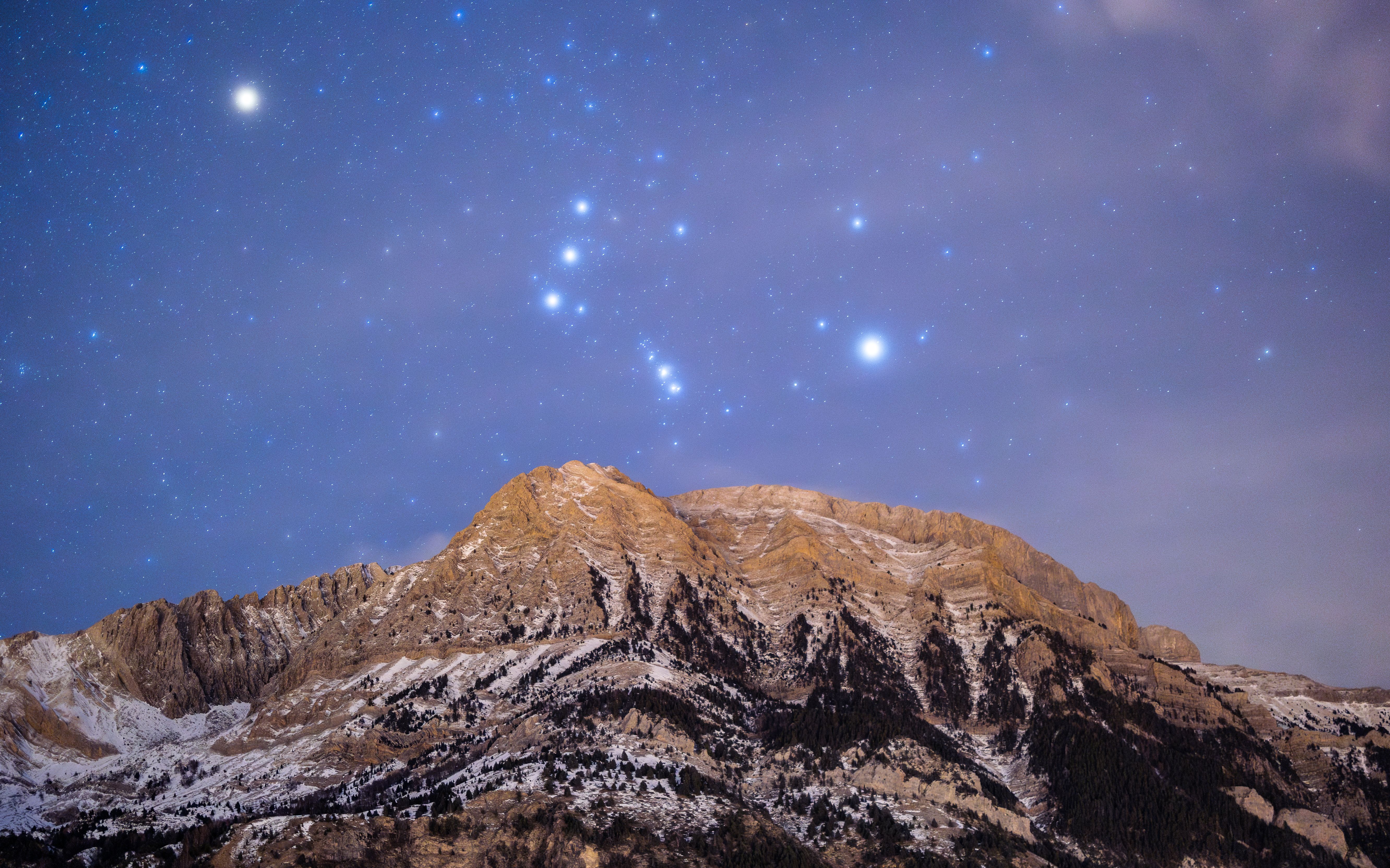 Stunning view of stars illuminating the snow-capped mountain peaks at night.