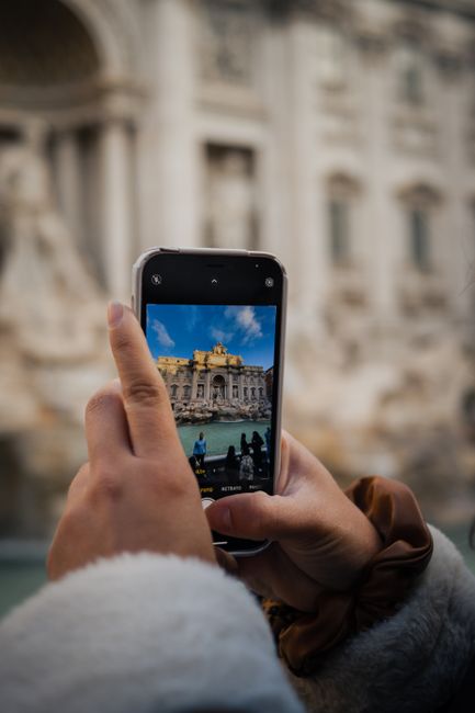 A person photographing the iconic Trevi Fountain in Rome using a smartphone, highlighting travel and tourism.