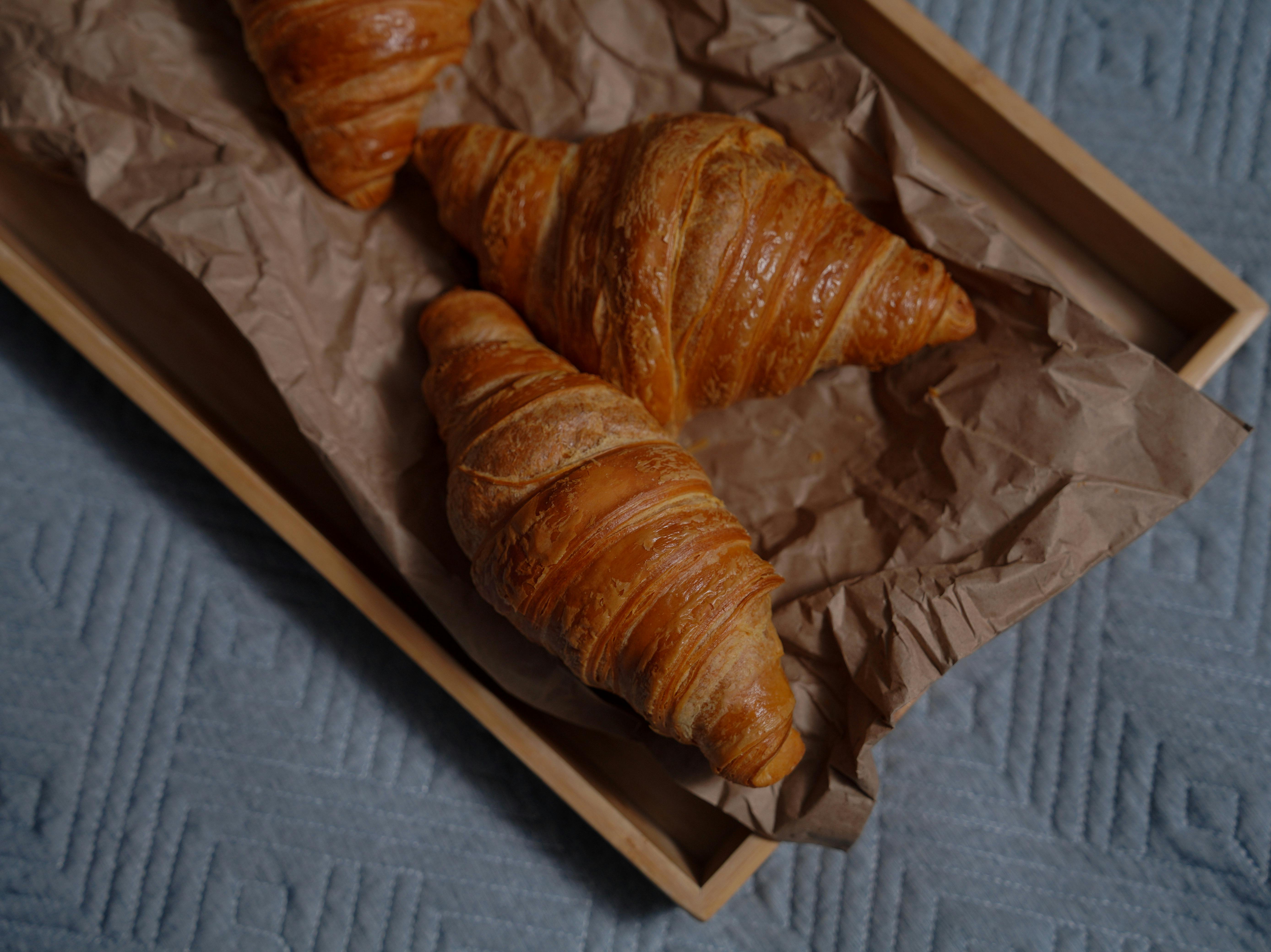 fresh croissants lying on brown paper on wooden tray