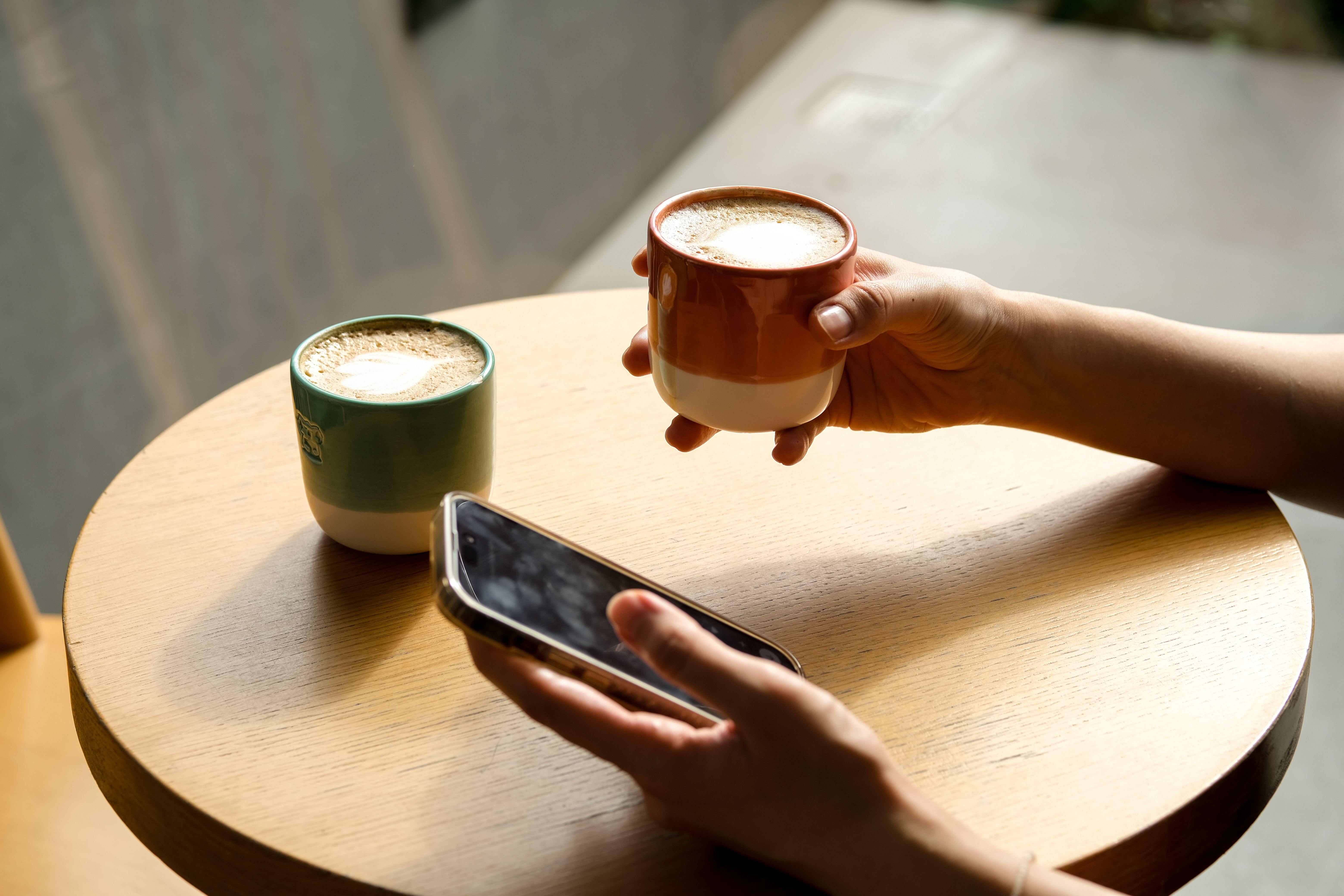 Hands holding coffee and phone on wooden table, Istanbul café.
