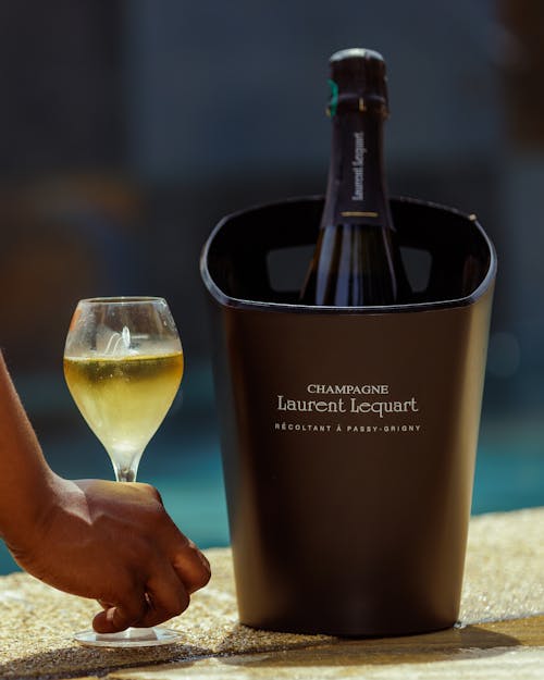 Hand Holding Glass of Champagne near Bucket with Bottle