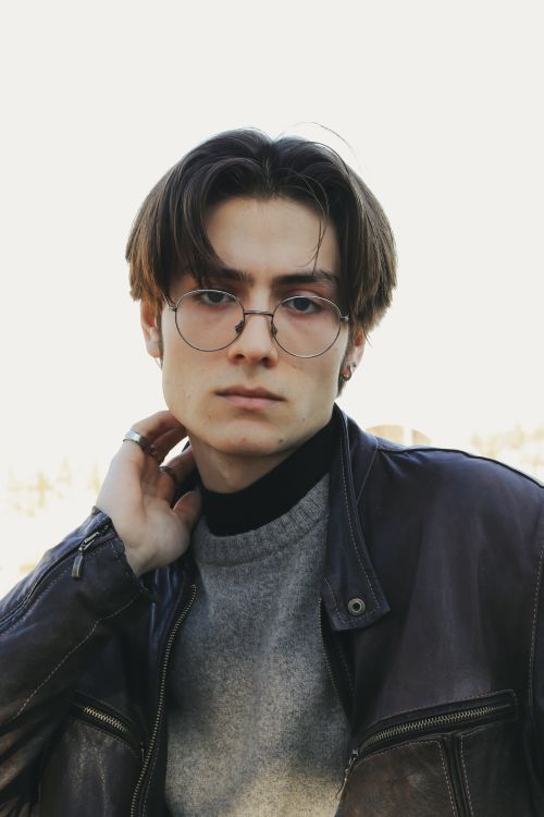 Free Stylish young adult male in glasses and leather jacket posing outdoors, embodying modern fashion trends. Stock Photo