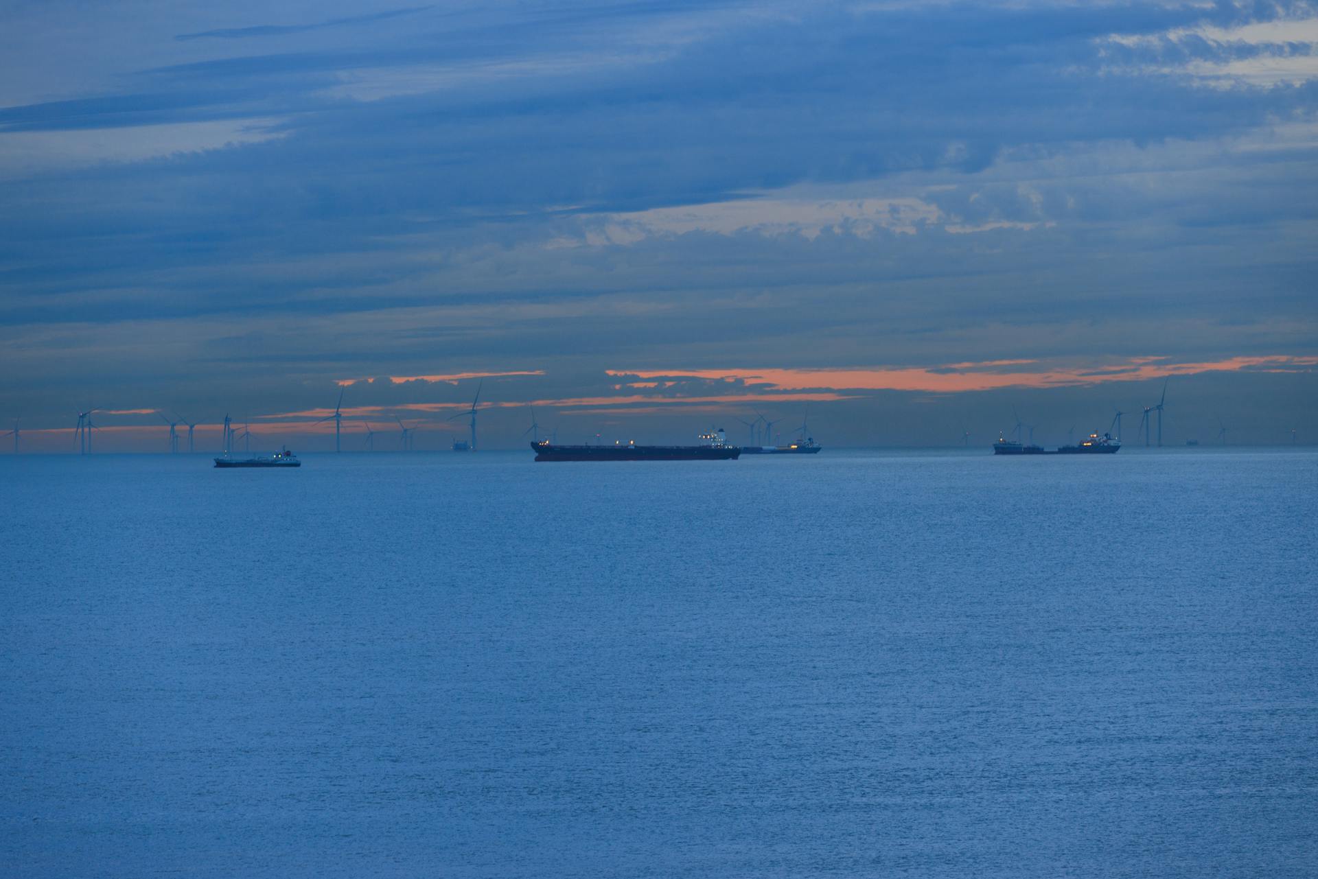 Serene ocean scene with cargo ships and wind turbines under a dramatic sunset sky.