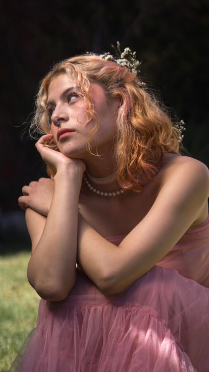 Young Woman in a Pink Dress and Flowers in Hair Sitting in a Garden ...
