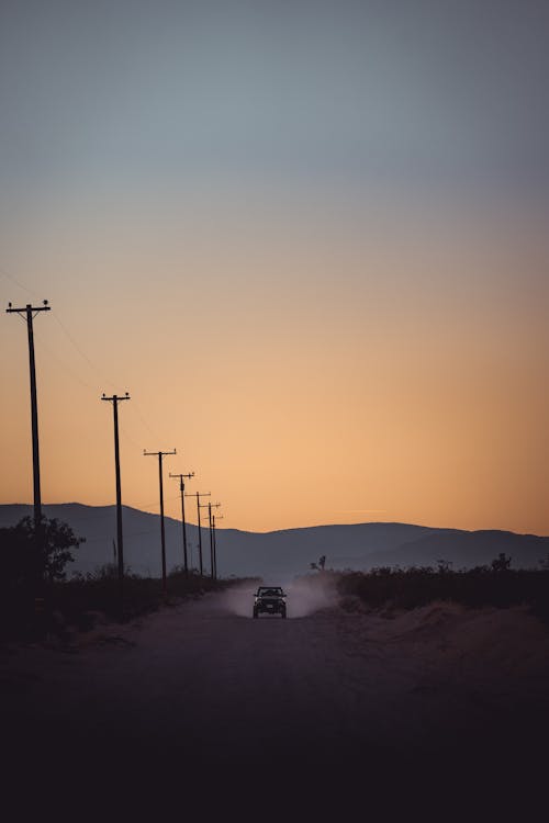 View of a Car on a Dirt Road with Silhouetted Mountains in Distance at Sunset