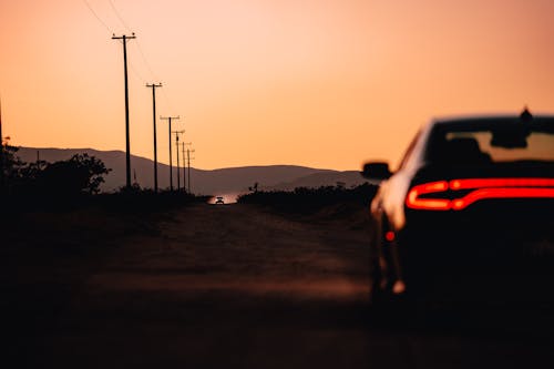 Defocused Photo of a Car on a Dirt Road with Silhouetted Mountains in Distance at Sunset