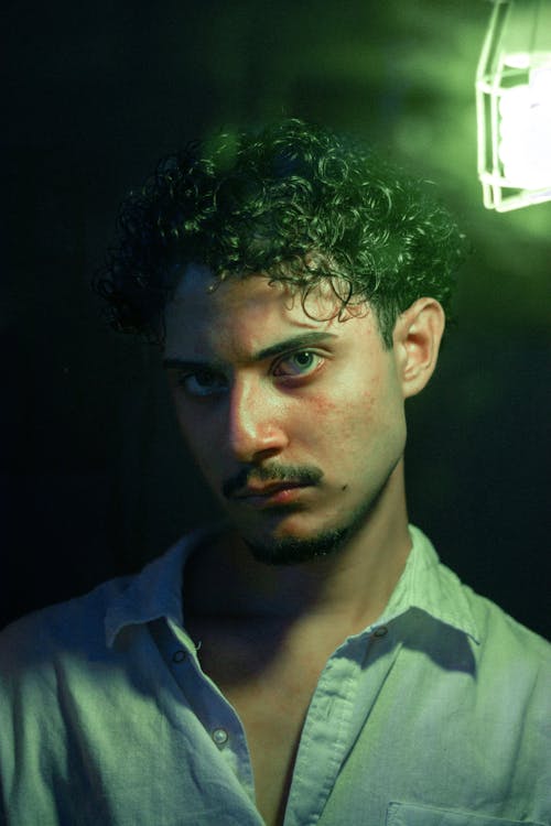 Portrait of a Young Man with Mustache and Curly Hair Standing next to a Green Light 