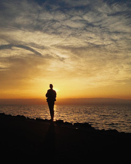 Silhouette of a Person Standing on the Shore at Sunset