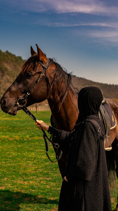 A woman in a black hijab is standing next to a horse